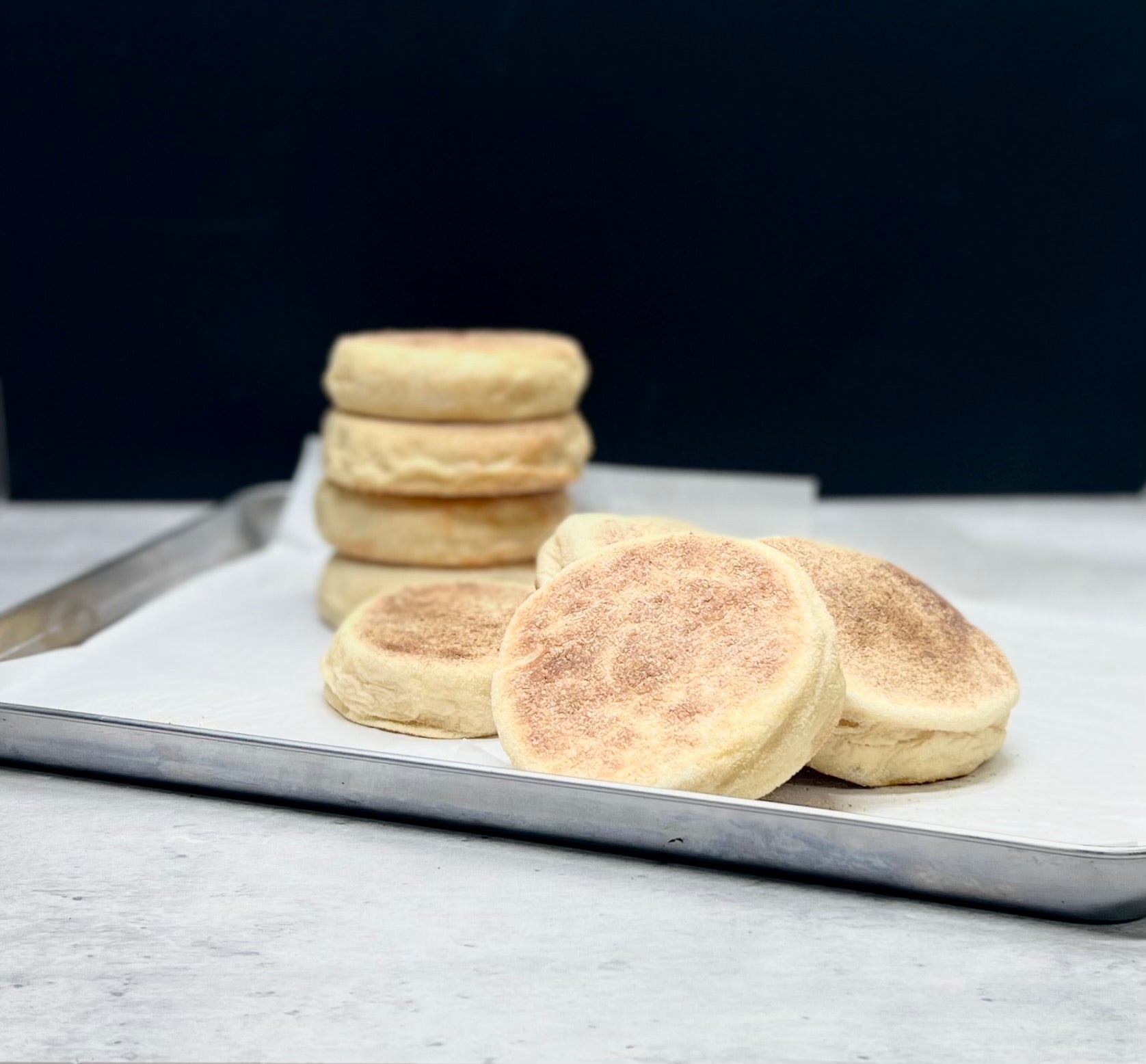 Stack of English muffins on a baking tray with a dark background