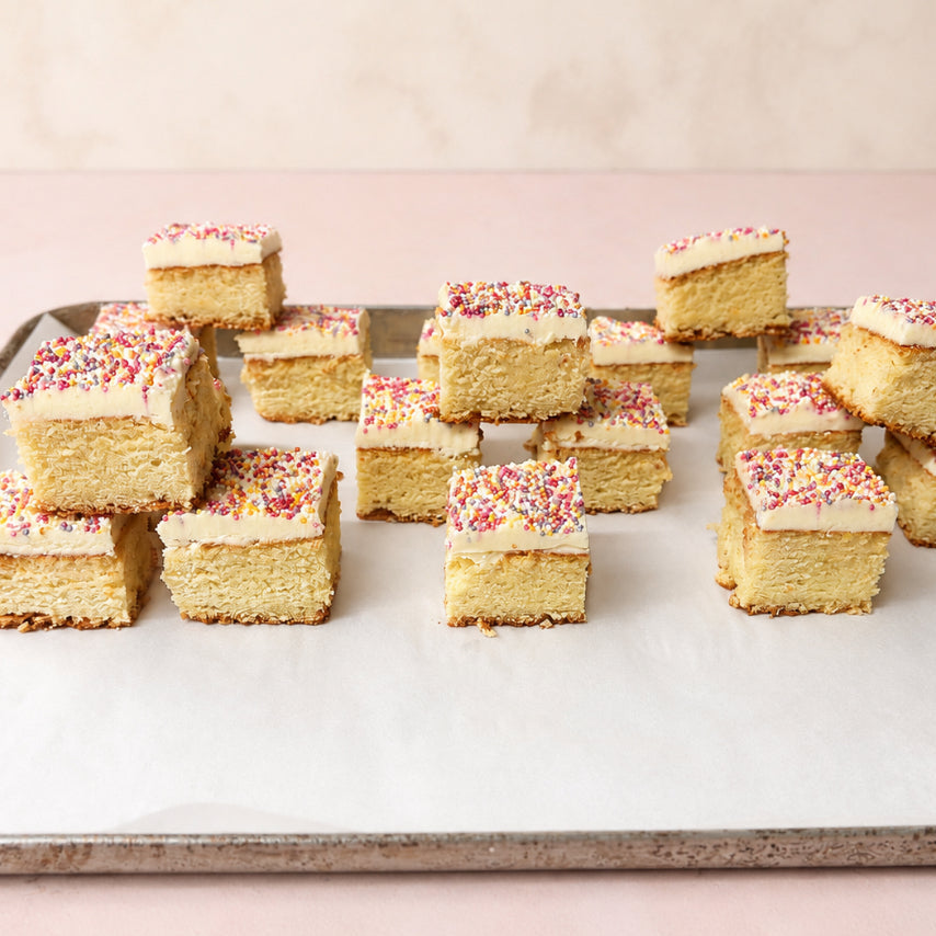 Sixteen vanilla Mini Dot Cakes topped with pink frosting and colourful sprinkles
